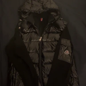 Moncler cardigan - Svart pufferjacka från Moncler med glansig yta och stickade svarta ärmar. Kan ta pengar eller om du har en annan jacka i bra skick vi kan absolut byta! Våga ställa frågor❤️✌️