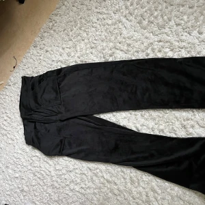 Svarta vida byxor i sammet - Säljer ett par svarta byxor i mjuk sammet med vida ben och hög midja. Byxorna har stora fickor framtill och en snygg, avslappnad passform. Perfekta för dig som gillar en trendig och bekväm stil.