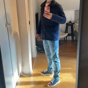 Blå pufferjacka Peak Performance S - Snygg mörkblå pufferjacka från Peak Performance i storlek S. Jackan har två stora fickor framtill med knappar, hög krage och dragkedja med knappslå. Perfekt för kyliga dagar och har en clean, stilren look. Priset är inte hugget i sten. Skriv om ni har funderingar. 