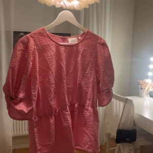 Rosa blus med puffärm - Supersöt rosa blus från Gestuz i storlek 38 med puffiga trekvartsärmar och knytdetalj vid ärmslutet. Blusen har en strukturerad, lätt glansig yta och dragkedja bak i nacken. Perfekt för dig som vill ha en feminin och trendig look. Hör gärna av er vid frågor eller funderingar! 💖(Dyrt märke därav priset.)