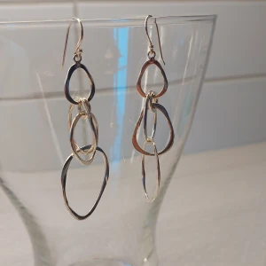 Unika handgjorda örhängen i äkta silver  - Unika silvriga örhängen med tre sammankopplade, oregelbundna ringar i metall. De är ca 7 cm långa och har en cool, modern design som verkligen sticker ut. Perfekta för dig som gillar statement-smycken och vill ha något som syns.