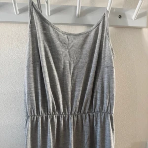 Grå långklänning med smala axelband - Enkel och stilren grå långklänning med smala axelband och resår i midjan. Klänningen har en rak passform och är tillverkad i ett mjukt, tunt material som känns skönt mot huden. I storlek XS, helt oanvänd.🤍