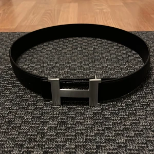 Svart bälte med H spänne  - Snyggt svart bälte med det ikoniska H spännet. Det är helt nytt och bilder på originalbox och certifikat kan skickas. 