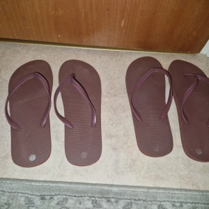 Flip-flops sandaler - Säljer två par bruna flip-flops med klassisk design. De har en enkel rem och platt sula, perfekta för varma dagar. Tillverkade i syntetmaterial och passar lika bra till stranden som till chill hemma. Enbart använda 1h inomhus. Priset är för båda paren men kan absolut köpas separata! Passar storlek 38 och 39