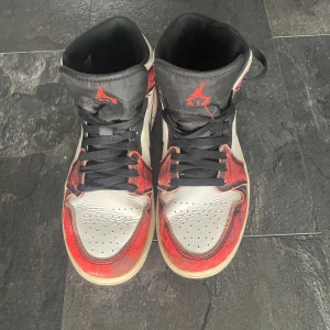 Nike Air Jordan 1 Chicago Highs - Säljer ett par Nike Air Jordan 1 Highs i klassiska Chicago-färger. Skorna har vit tåbox och sidor, röda paneler med svart Swoosh och svarta snören. Ovandelen är i skinn med perforerad tå och svart plös med röd Jumpman-logga. Perfekta för dig som gillar streetwear och sneakerskultur.