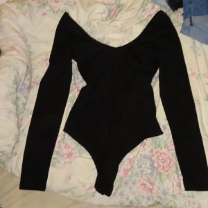 Svart ribbad bodysuit - Säljer en svart ribbad bodysuit  med lång ärm. Toppen har en tight passform och är tillverkad i ett stretchigt material som sitter snyggt på kroppen. Perfekt för dig som vill ha en stilren och trendig look.