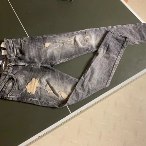 Grå slitna slim jeans Calvin Klein - Säljer ett par gråsvarta skinny jeans från Calvin Klein med slitningar och hål på låren och knäna. Jeansen har en tvättad look, klassiska fem fickor och tydlig logga på bakfickan. Snygg passform som sitter bra hela vägen ner.