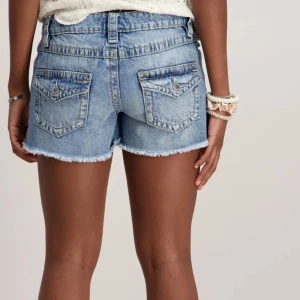 Blå jeansshorts med fransad kant - Snygga blå jeansshorts med fransad kant och två bakfickor med lock och knappar