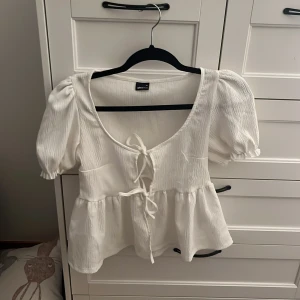 Vit blus med knyt från Gina Tricot - Supersöt vit blus från Gina Tricot med puffiga korta ärmar och två knyt framtill. strlk XS