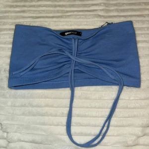 Blå bandeau tubtopp från Gina Tricot - Säljer en blå bandeau tubtopp från Gina Tricot med snygg snörning framtill. Mjuk och stretchig i bomullsmix.