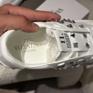 Valentino Rockstud vita sneakers - Snygga vita Valentino Garavani Rockstud Untitled sneakers i skinn med ikoniska silverfärgade nitar. Klassisk låg modell med snörning och platt sula. Perfekta för dig som vill sticka ut med exklusiva detaljer och stilren design.