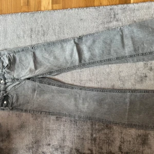 Grå jeansbyxor med fickdetaljer - Snygga grå jeansbyxor från gina tricot med boot cut och coola fickor med lock och knapp bak. Klassisk femficksmodell framtill och silverfärgade knappar. Perfekta för dig som gillar en avslappnad men stilren look.