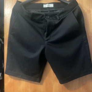 Svarta shorts från Lindbergh White - Stilrena svarta shorts från Lindbergh White med klassisk passform och dragkedja framtill. Shortsen har diskreta fickor och är tillverkade i ett mjukt, vävt material som känns bekvämt mot huden. Perfekta för en clean och enkel look under varma dagar.