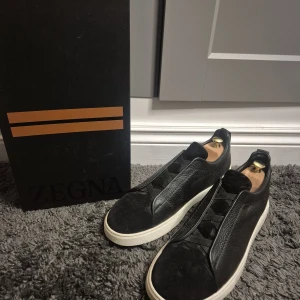 Zegna Triple Stitch svarta sneakers - Snygga Zegna Triple Stitch sneakers i svart skinn och mocka med vita sulor. Köpta I Zegna affären utan för Las Vegas usa. Ikoniska elastiska band över vristen och diskret Zegna-logo bak på hälen. Kommer med originalpåse och box. Perfekta för dig som gillar stilrena och lyxiga sneakers. Pris kan diskuteras.💕