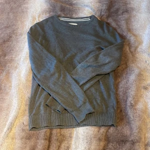 Mörkgrå stickad tröja från Pier One - Snygg mörkgrå stickad tröja från Pier One med rund halsringning och ribbade muddar vid ärmslut och nederkant. Perfekt för lager-på-lager och enkel att matcha med jeans eller chinos. Klassisk och stilren modell som funkar året runt.