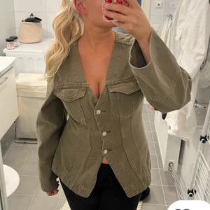 Olivgrön jeansjacka med v-ringning - Snygg olivgrön jeansjacka från Gina tricot med markerad midja, storlek S.