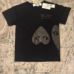 Svart Comme des Garçons Play t-shirt - Säljer min sprillans nya Comme des Garçons tisha med det ikoniska hjärtögon-trycket i mörkgrått på både fram- och baksidan. Tillverkad i mjuk bomull för en skön känsla. Perfekt för dig som gillar streetstyle och coola prints. Skriv vid minsta fundering! 