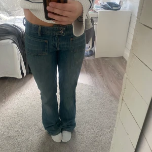 Blå bootcut jeans från Gina Tricot - Snygga blå jeans från Gina Tricot med låg midja och bootcut-ben. Jeansen har stora fickor fram, dubbla knappar i midjan och klassisk denimlook. Perfekta för dig som gillar en retro vibe och vill ha ett par jeans som sticker ut lite extra.