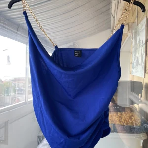 Blå och grön linnetopp med guldkedjor - Två snygga linnetoppar från SHEIN i blått och grönt. Båda har tunna axelband i guldfärgad kedja och en draperad, lös passform framtill. Säljer båda för 50kr