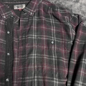 Rutig skjorta från Tommy Hilfiger  - Snygg rutig skjorta från Hilfiger Denim i mörka toner av grått och vinrött. Skjortan har klassisk krage, två bröstfickor med knappar och långa ärmar. Tillverkad i mjuk bomull, perfekt för dig som gillar en chill och stilren look.