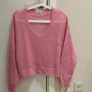  Ny Rosa stickad tröja från MNG - Mysig rosa stickad tröja från MNG med v-ringad hals och långärmad design. Tröjan är tillverkad i en mjuk ullblandning och har en lätt fluffig struktur. Perfekt för att ge din outfit en färgklick och skön känsla under kyliga dagar.