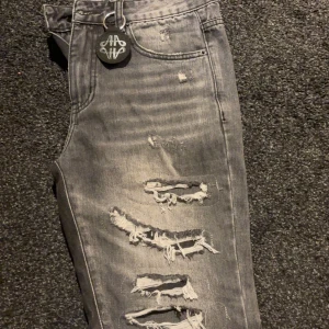  jeans från Amicci  - Säljer ett par grå jeans från Amicci med kraftiga slitningar och ripped detaljer längs hela framsidan. Slut sålda på hemsidan.  Modellen har fem fickor, normal passform och klassisk jeansknäppning. Perfekt för dig som gillar en edgy streetstil.