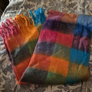 Färgglad rutig halsduk med fransar - En stor och fluffig halsduk med rutigt mönster i starka färger som blå, orange, rosa och grön. Halsduken har långa fransar i olika färger och är perfekt för att liva upp vinterlooken. Materialet känns mjukt och värmande, perfekt att svepa in sig i kalla dagar.
