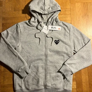 Grå Comme Des Garçons Play Zip Hoodie. - Grå Comme Des Garçons Play Zip Hoodie.  Skick 10-10 aldrig använd ✅ Storlek S 👕 Material bomull 🧶 Färg grå 🎨 Mått B47/ L62cm Fraktar senast dagen efter 🚚💨  Priset går att diskutera vid en snabb och smidig affär. Det är bara att höra av dig vid frågor.