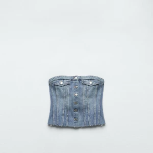 Blå denim korsett med knappar - Säljer en snygg blå denim korsett med knappar framtill och rå kant nertill. Toppen har dekorativa sömmar och två små fickor med lock upptill. Perfekt för dig som vill ha en edgy och trendig look.