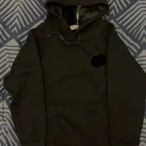 Svart hoodie med mjuk fleecefoder - Svart hoodie med mjukt fleecefoder i huvan, perfekt för kyliga dagar. Tröjan har snörning vid huvan och en stor magficka framtill. Stilren och enkel design som funkar till många olika looks. Snyggt och bekvämt plagg för dig som gillar streetwear. Skriv vid frågor om märke!!!