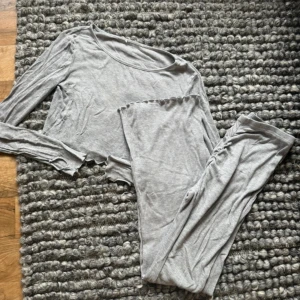 Grå croppad långärmad tröja - Säljer en ljusgrå croppad långärmad tröja i mjukt och stretchigt bomullsmaterial. Tröjan har råa kanter och en enkel, stilren design som passar perfekt till chill dagar. Matchande byxor med rynkdetalj bak ingår.