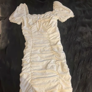 Vit omlottklänning med puffärm - Superfin vit kortklänning med puffärmar och broderade detaljer. Klänningen har omlottknytning vid halsen och är lätt rynkad längs sidorna för en snygg siluett. Storlek S