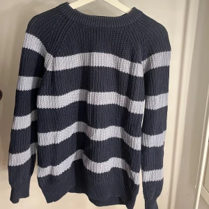 Randig stickad tröja i mörkblått och vitt - Säljer en stickad tröja med breda vågiga ränder i mörkblått och vitt. Tröjan har ribbad struktur, rund hals och långa ärmar. Oversized 