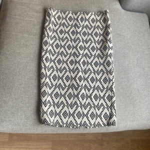Vit och svart mönstrad kjol,S - Kort kjol från Stradivarius i storlek S,stretch med ett coolt geometriskt mönster i svart och vitt. Kjolen har rak passform och är tillverkad i ett tjockare bomullsmaterial med elastisk midja för extra komfort. Perfekt för dig som gillar grafiska prints.mycket bra skick.använd 1 gång.