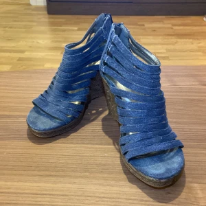Blå denim kilklack sandaler från Duffy - Snygga sandaler från Duffy i blå denim med kilklack och öppna tår. Skorna har flera remmar och är ett riktigt bra par ”statement” klackar.