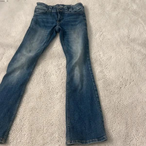 Blå bootcut jeans från H&M, stl 152 - Snygga blå bootcut jeans från H&M med låg midja och justerbar midja. Jeansen har klassisk femficksdesign med ficklock och silverfärgade knappar bak. 