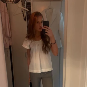 Vit blus med kort ärm - Säljer en söt vit blus med korta ärmar och rund halsringning. Blusen har en lös passform och fina veck framtill.