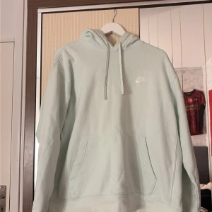 Ljusblå hoodie från Nike XL - Snygg ljusblå hoodie från Nike i storlek XL. Tröjan har klassisk huva med snörning, stor magficka och Nike-logga broderad på bröstet. Mjuk insida och ribbade muddar vid ärmslut och nederkant. Perfekt för chill eller streetwear.