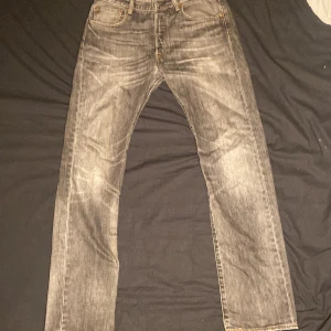 Levi's 501 grå straight jeans - Säljer ett par Levi's 501 jeans i grå tvättad färg med klassisk straight fit. Jeansen har fem fickor, knappgylf och den ikoniska läderpatchen bak. Perfekt för dig som gillar tidlös stil och vill ha ett par jeans som funkar till allt.