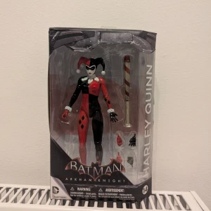 Batman Arkham Knight Harley Quinn Action Figure - Snygg Harley Quinn actionfigur från Batman Arkham Knight, i originalförpackning. Figuren har flera utbytbara händer och tillbehör, inklusive en batong. Den är öppnad och har stått på en hylla, men allt är i jättefint skick. Är villig att pruta!