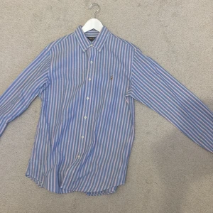 Randig skjorta från Polo Ralph Lauren - Säljer en klassisk skjorta från Polo Ralph Lauren i blått, vitt och rosa med smala ränder. Skjortan har button-down krage, broderad logga på bröstet och knäppning framtill. Perfekt passform med långa ärmar och custom fit. Helt ny och oanvänd. Lappen åkte av när jag testa den. Har kvar kvitto och lapparna. För fler bilder hör gärna av dig!😊