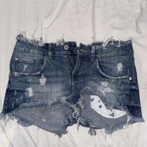 Blå slitna jeansshorts från Zara - Blåa jeansshorts med rufsig kant, dessutom fickor med hjärtdetaljer på.