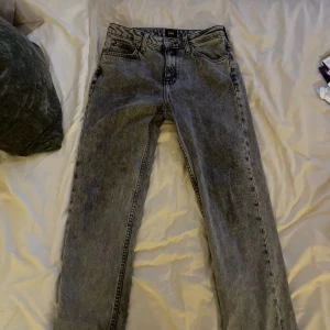 Grå Lee jeans med straight fit W28 L31 - Säljer ett par grå jeans från Lee med klassisk femficksdesign och raka ben. Jeansen har en snygg tvättad look, metallknapp med Lee-logga och bälteshällor. Passar dig som gillar tidlös stil och vill ha ett par jeans med cool vintagekänsla. Nyskick, W28 L31 