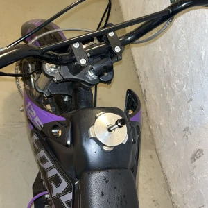 DirtPro 125 Racing fiddy - Snygg DirtPro 125 Racing cross med lila och svart design. Utrustad med grova däck, sportavgassystem och racingdetaljer. Cykeln ser välvårdad ut med minimalt slitage, perfekt för både nybörjare och erfarna förare. Motorn och komponenter ser rena ut.