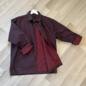 Mörkröd skjorta från Selected L - Snygg skjorta från Selected i storlek L, mörkröd med vinröda toner. Klassisk krage, långa ärmar och knappar framtill. Tillverkad i mjuk bomull som känns skön mot huden. Perfekt för dig som gillar stilrena och enkla plagg med lite edge.