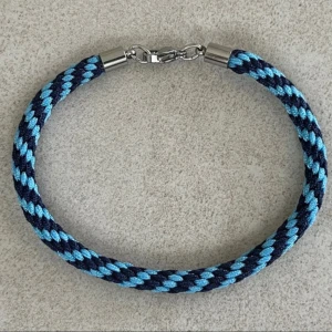 Djurgården DIF armand 19cm - Priset på armbandet är fast, knappen ”prisförslag” går inte att dölja.  Handflätat armband i mörkblått ljusblått med spänne i rostfritt stål, ca 19cm. Det har en inflätad rostfri ståltråd som gör att det inte tänjer sig vid användning.