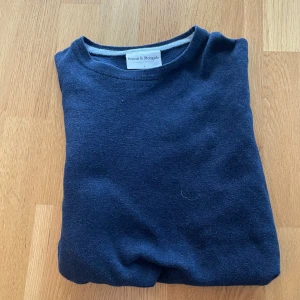 Mörkblå stickad tröja Bruun & Stengade - Mörkblå stickad tröja från Bruun & Stengade i storlek S. Klassisk modell med rund halsringning och långa ärmar. Tröjan har ribbade muddar vid ärmslut och nederkant, perfekt för lager-på-lager under höst och vinter.