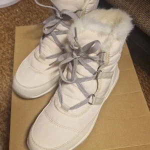 Sorel - Vita vinterstövlar  - Snygga vita vinterboots med grå snörning från Sorel med fluffig päls runt skaftet och på insidan. Bootsens ovandel är tillverkad i syntetskinn, med en rubber sula och rund tå. Perfekta för kalla dagar med sin varma och mjuka insida. Kängorna användes bara en gång. Det syns på. 