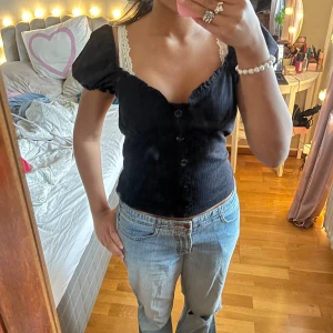 Svart blus med puffärm från NA-KD - Supersöt svart blus från NA-KD med puffiga korta ärmar och v-ringad hals. Blusen har knappar framtill och är lätt ribbad i materialet💘