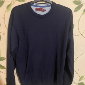 Mörkblå stickad tröja Coney Island XL - Mörkblå stickad tröja från Coney Island i storlek XL men den sitter mer som en s/m. Tröjan har rund hals och långa ärmar, perfekt för dig som gillar enkel och stilren design. Materialet är mjukt och skönt, och den passar dig som vill ha en klassisk look med lite extra edge.